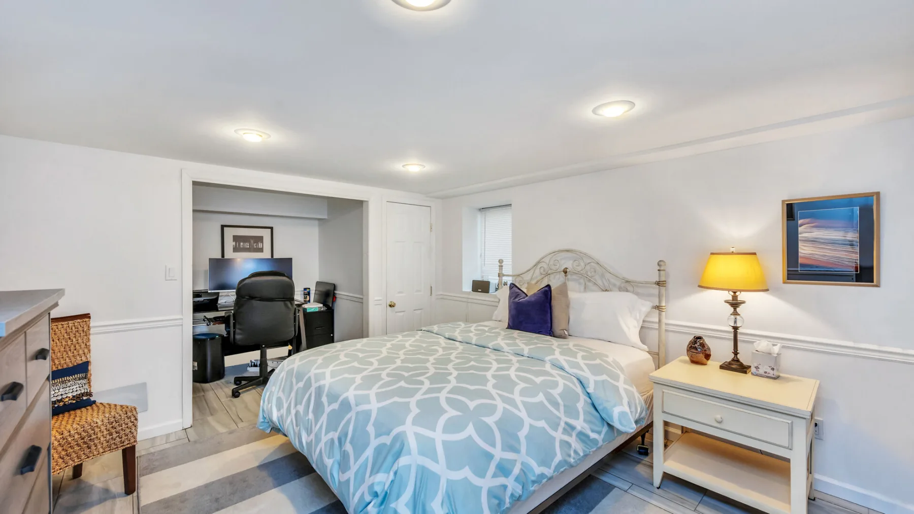 Un dormitorio con una cama cubierta con ropa de cama azul estampada y un escritorio en el rincón contiguo.