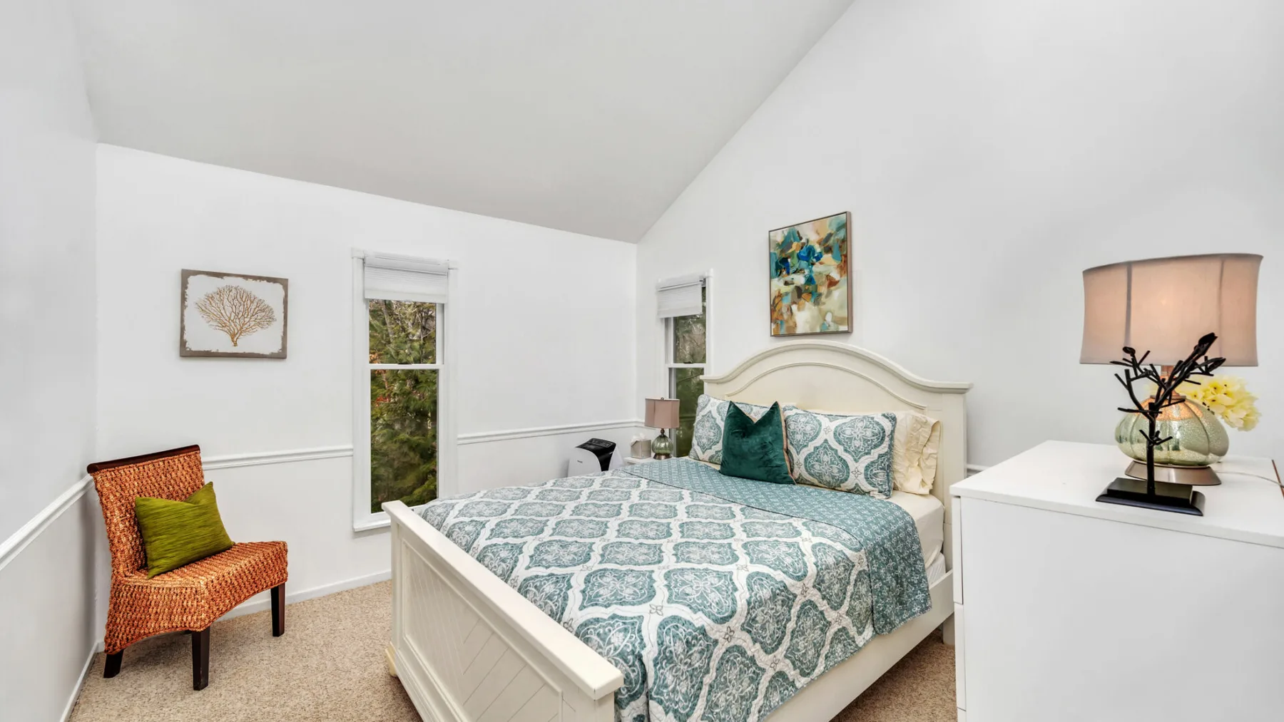 Un dormitorio luminoso con una cama estampada y una silla decorativa de mimbre.