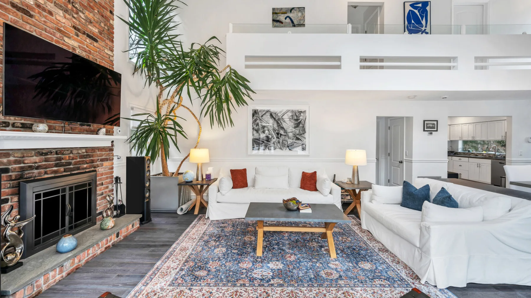 A bright living room with white seating, a fireplace, and a patterned rug.