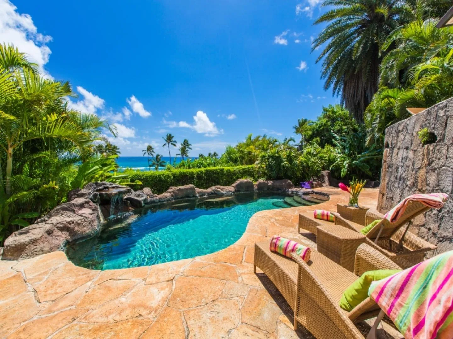 A turquoise swimming pool sits among tropical plants, with lounge seating beside it.
