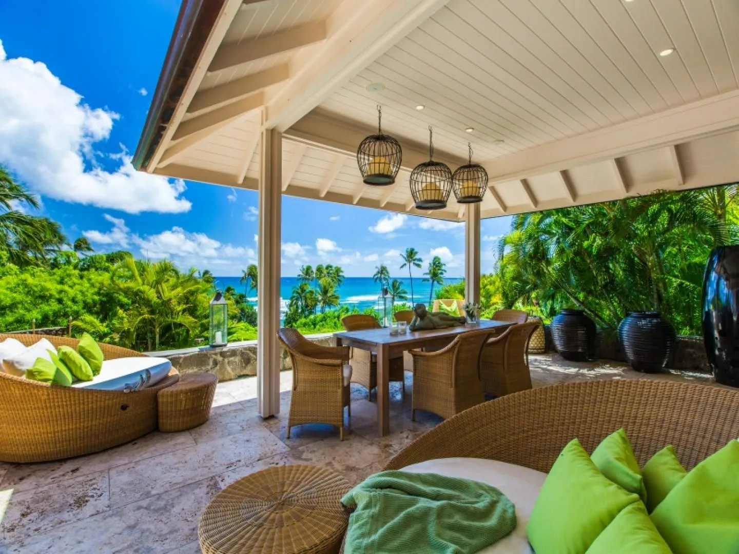 A covered outdoor dining and seating area overlooks tropical greenery and the ocean.