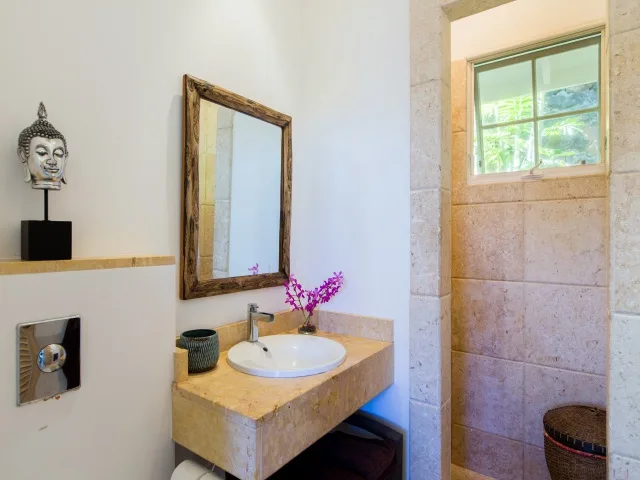 A bathroom vanity with a basin and mirror sits beside a tiled shower area.