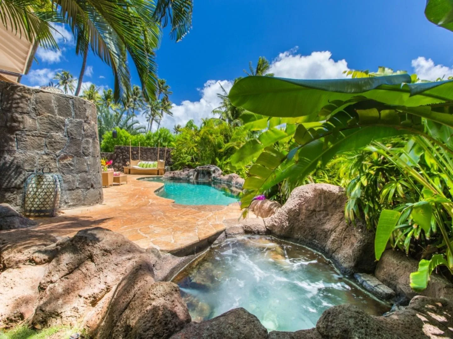 A tropical outdoor pool and bubbling spa sit among large rocks and lush plants.