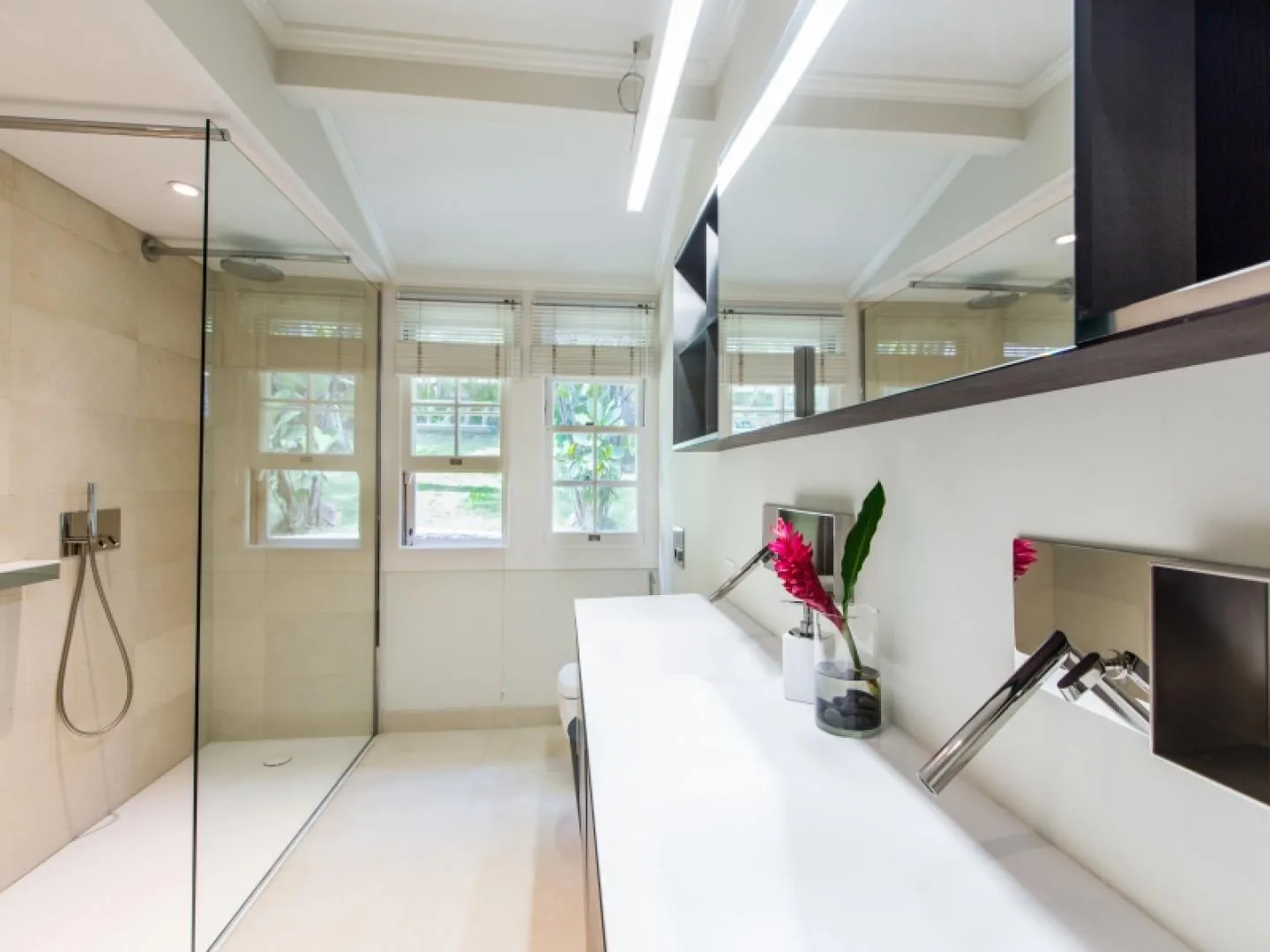 A bright bathroom with a glass shower and a long white vanity.