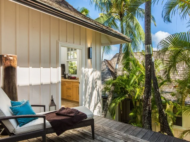 An outdoor deck with seating overlooks palm trees beside a light-colored building.