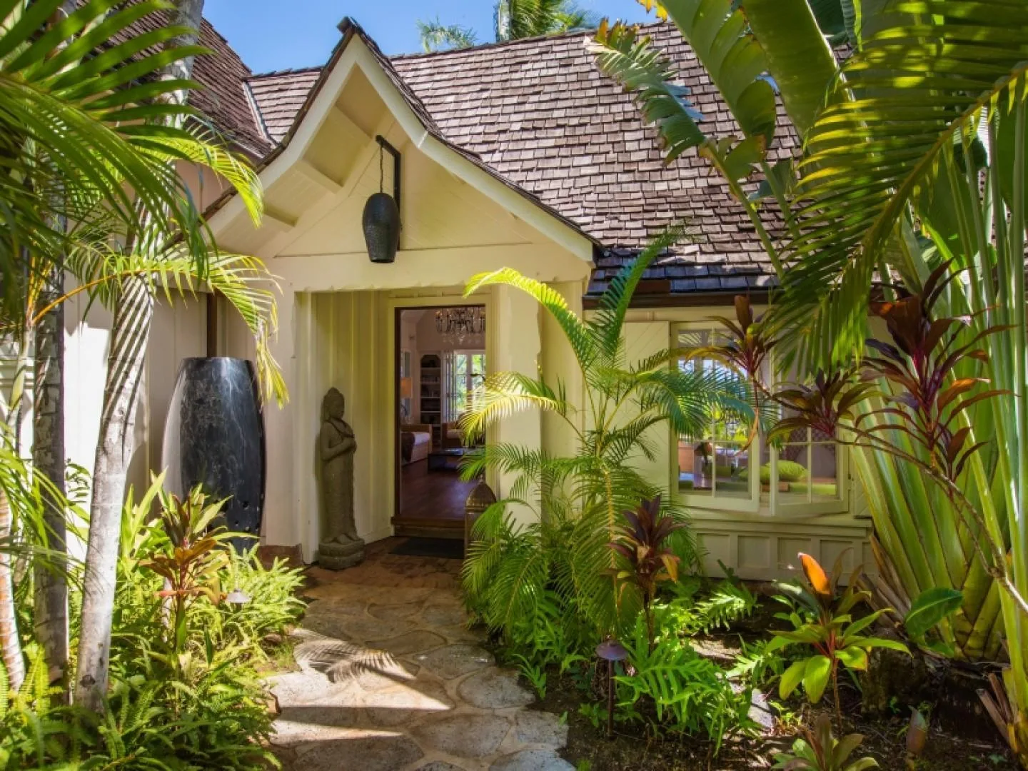 A tropical house entrance with a stone path and lush plants.
