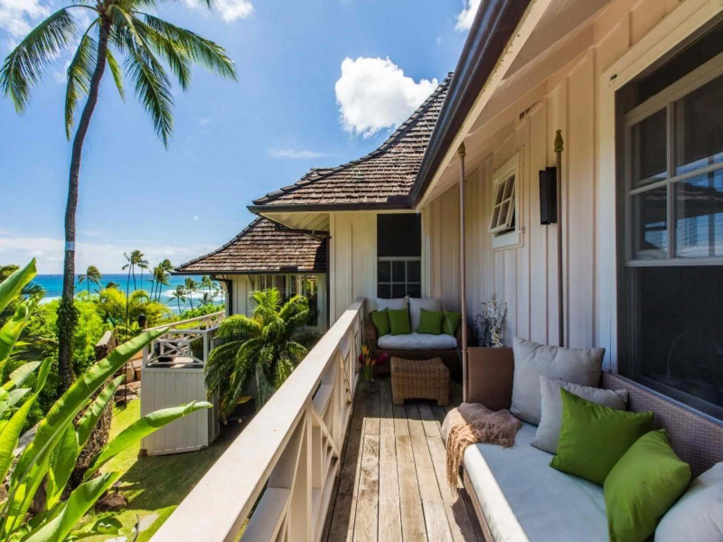 A covered balcony has cushioned seating and views of palm trees and the ocean.