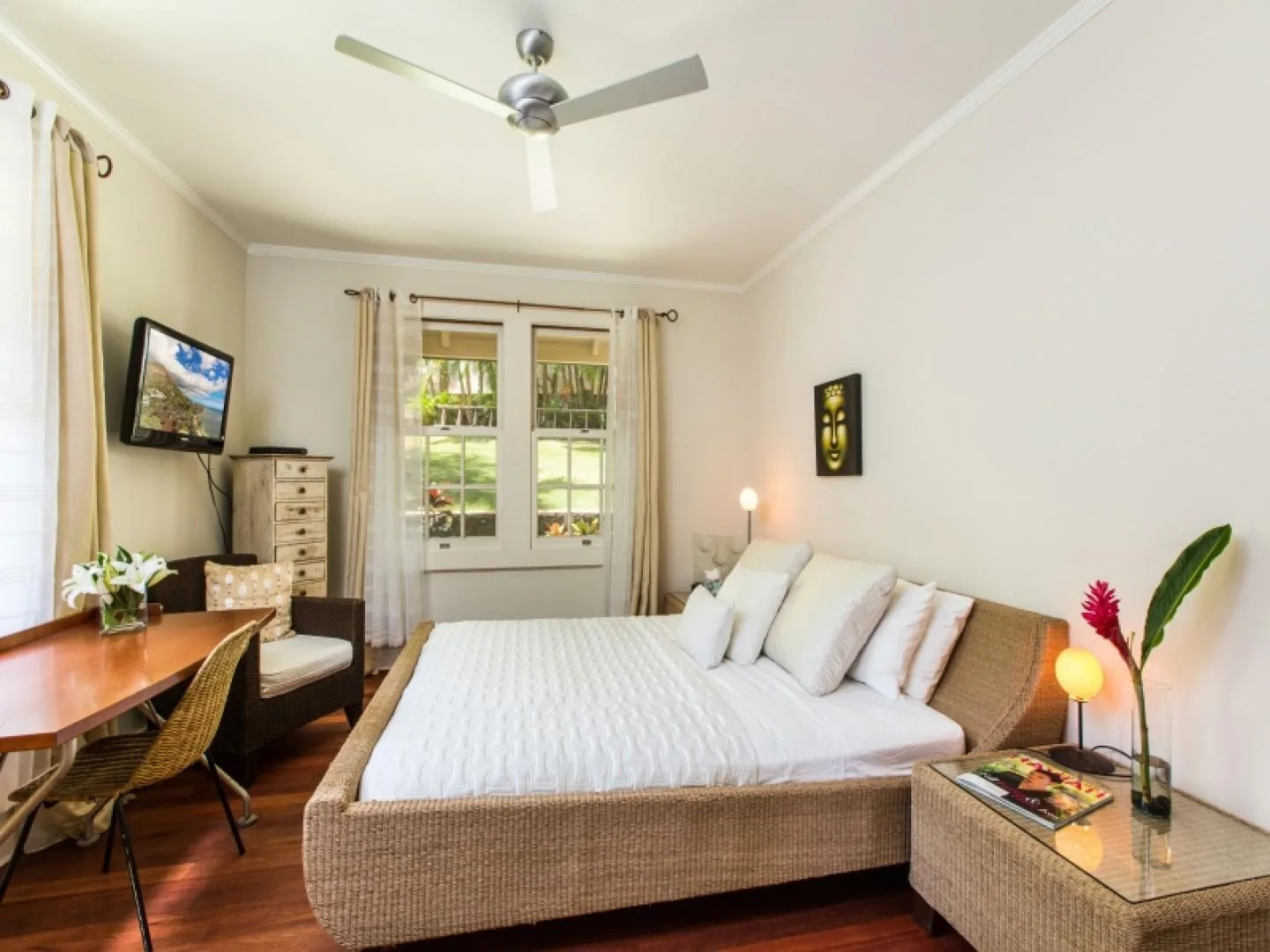 A bright bedroom with a large bed, windows, and a ceiling fan.