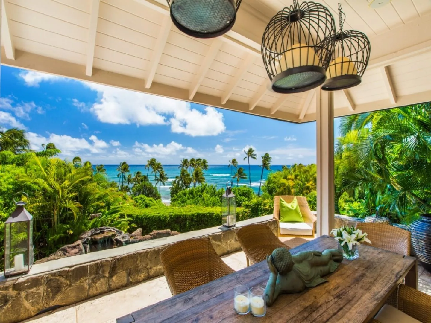 A covered outdoor seating area overlooks lush greenery and the ocean.