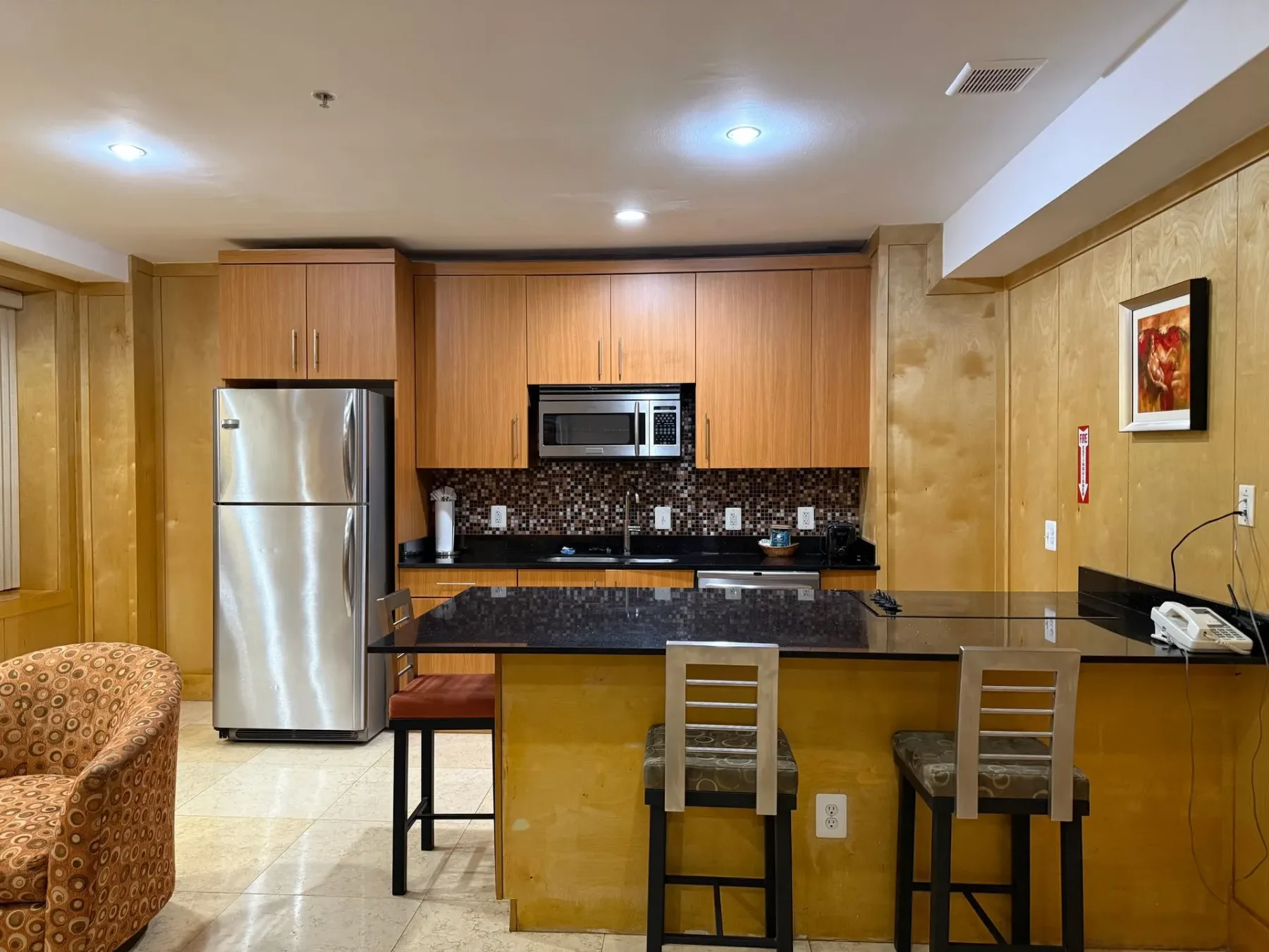Cocina con refrigerador, armarios y taburetes de bar.