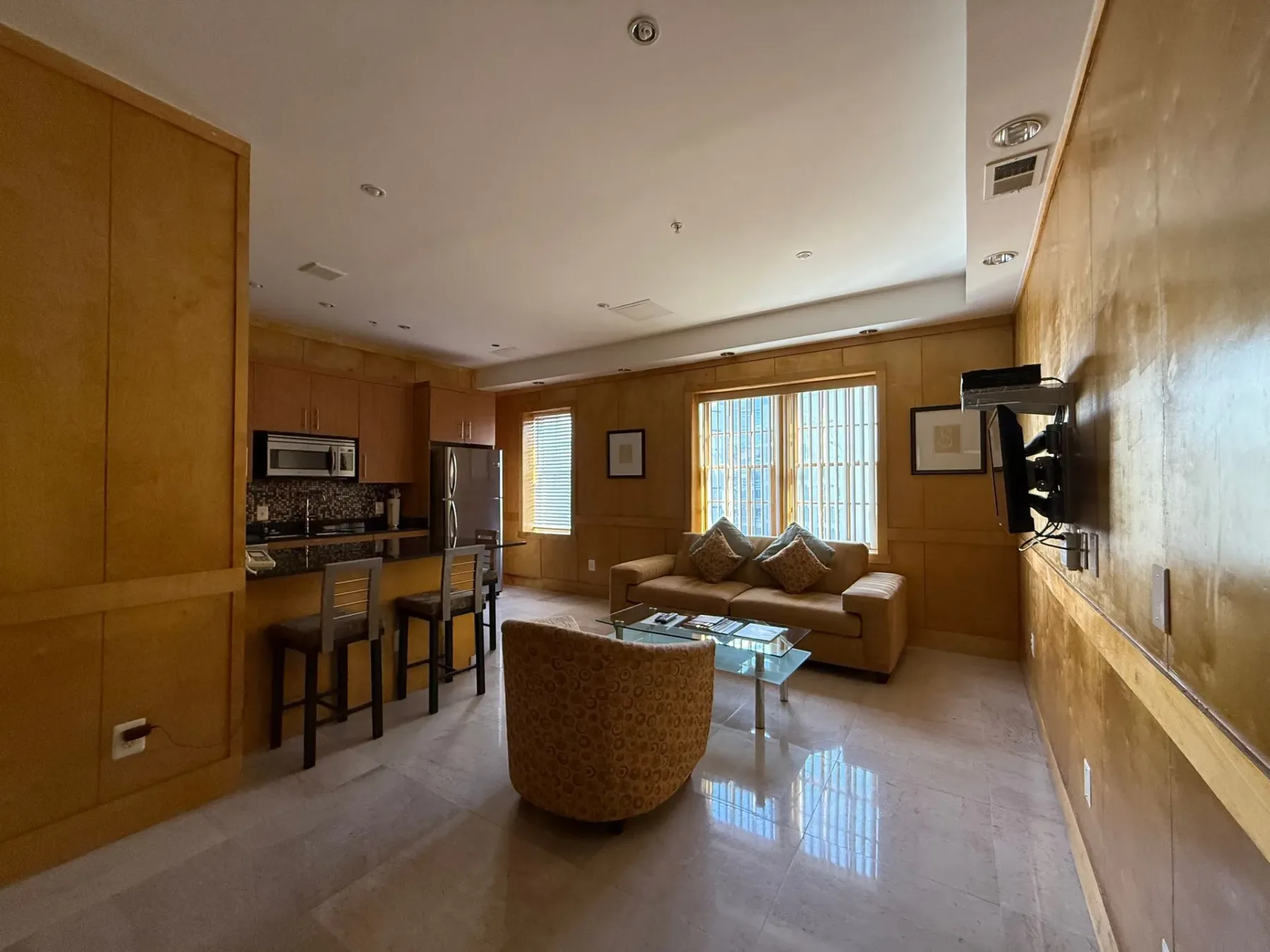 Sala de estar con cocina pequeña, sofá y taburetes de bar.