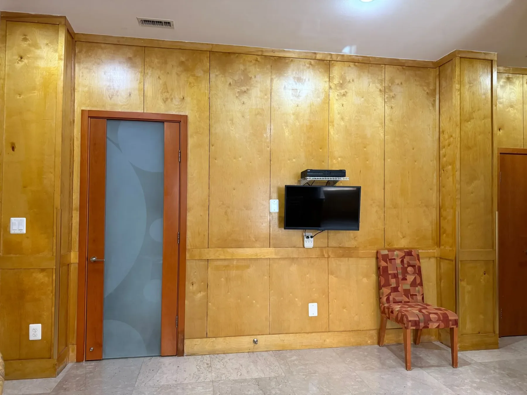 Habitación con revestimiento de madera, televisor y silla.
