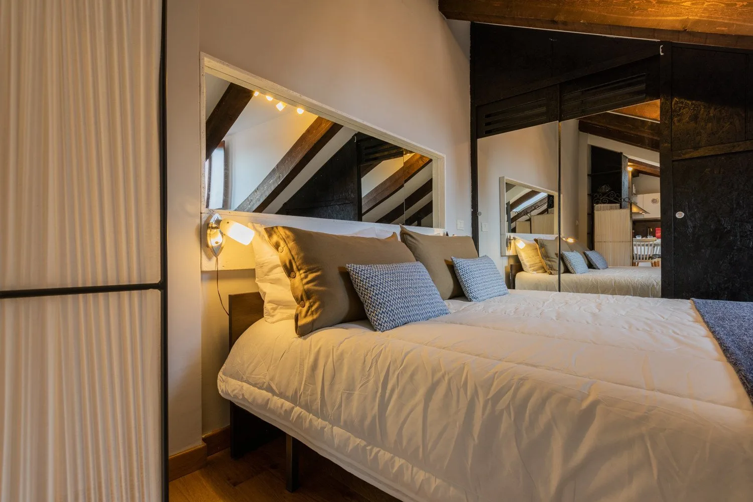 A bedroom with a bed, pillows, and mirrored wall panels.
