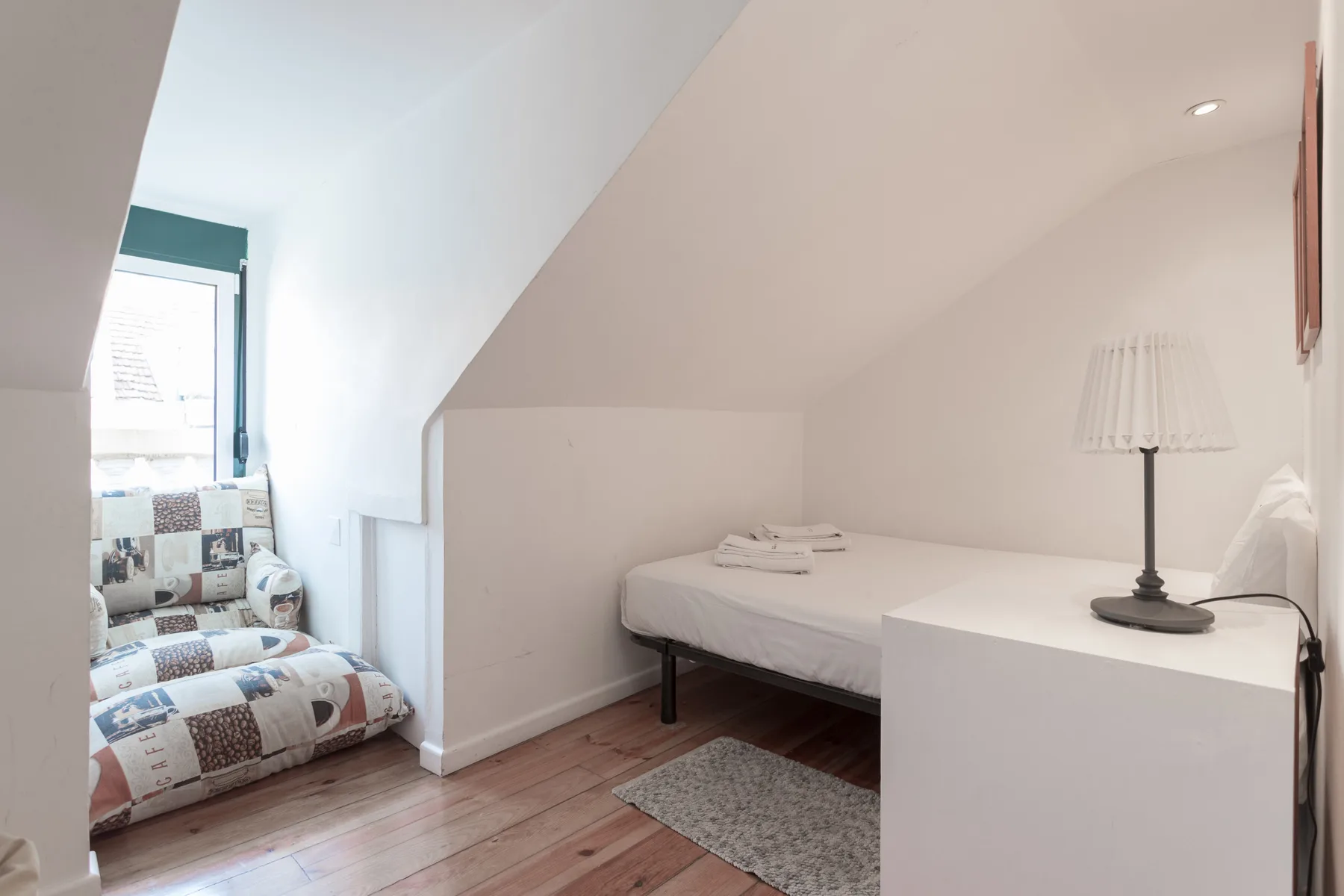 Un dormitorio pequeño con una cama, un sillón estampado y una lámpara de mesa.