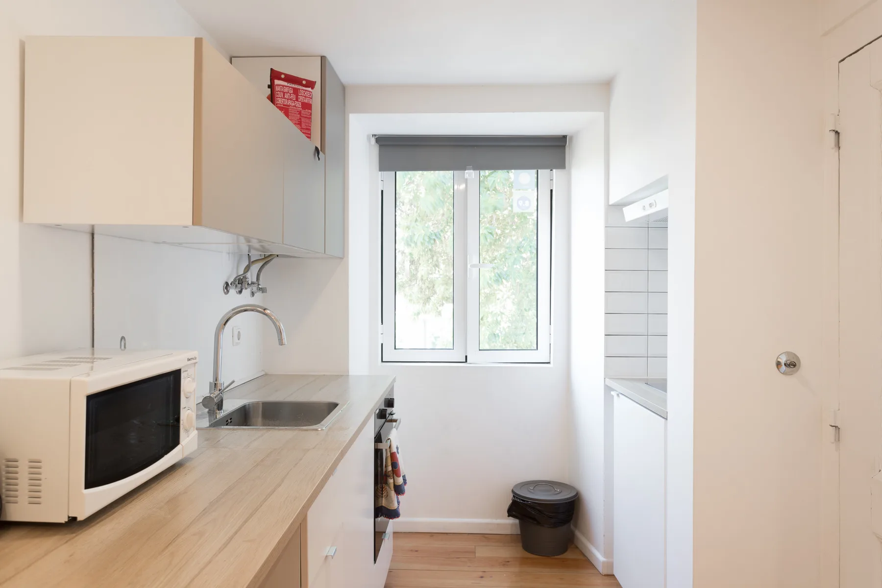 Una cocina compacta con un microondas sobre la encimera y una ventana al fondo.