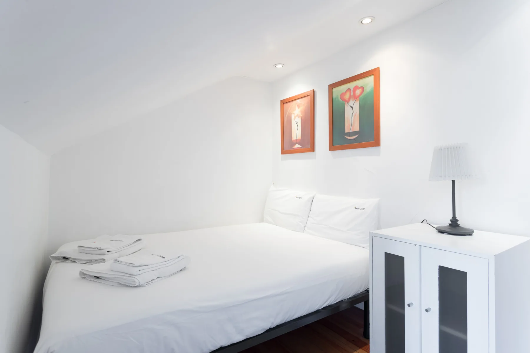 Un dormitorio luminoso con ropa de cama blanca y cuadros sobre la cama.