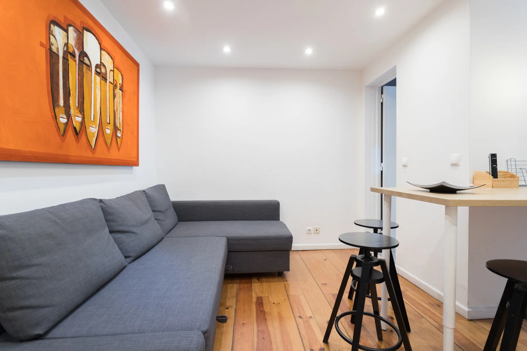 Una sala de estar con asientos grises, suelo de madera y una pequeña barra.
