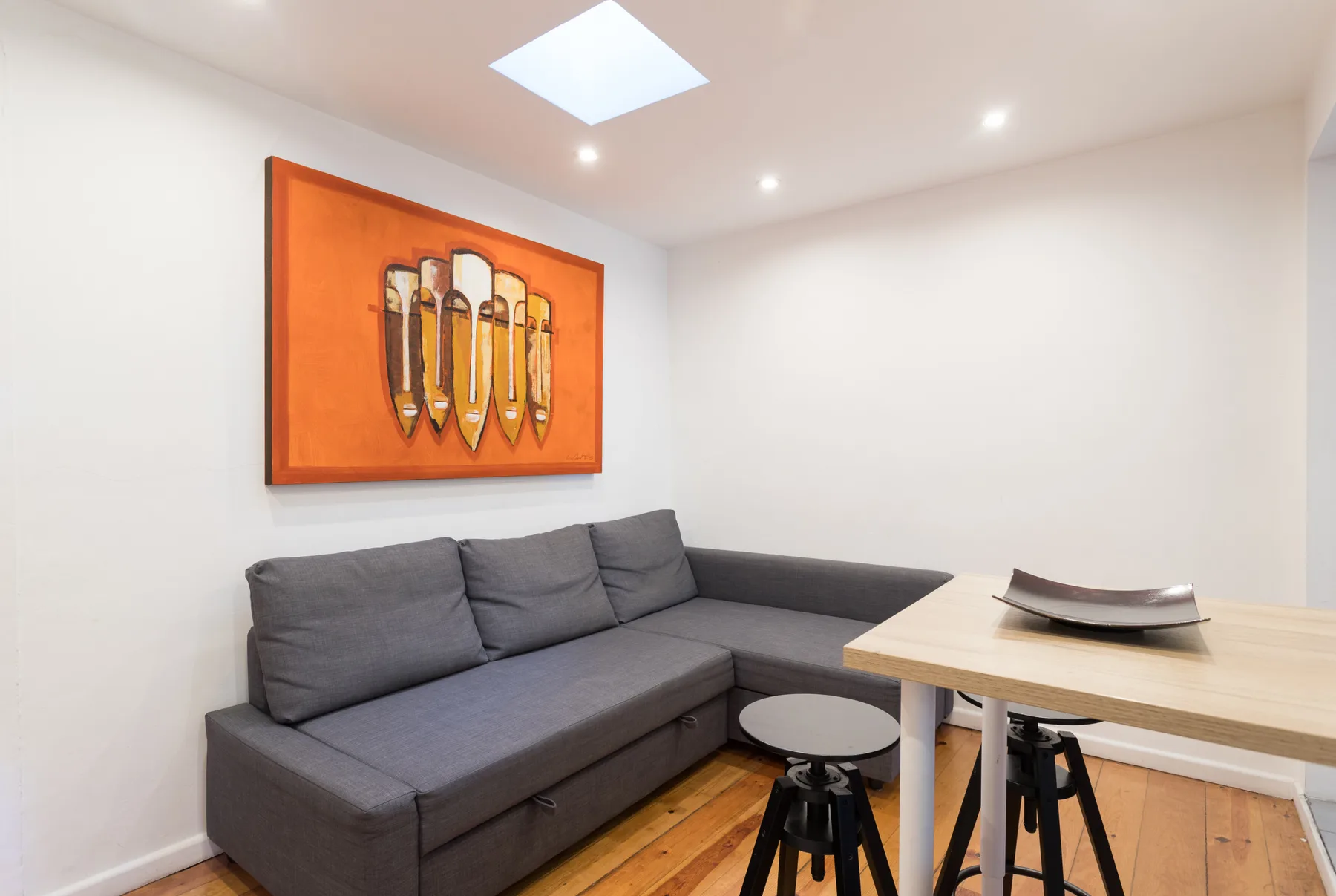 Una sala de estar con un sofá seccional gris, una mesa y arte colorido en la pared.
