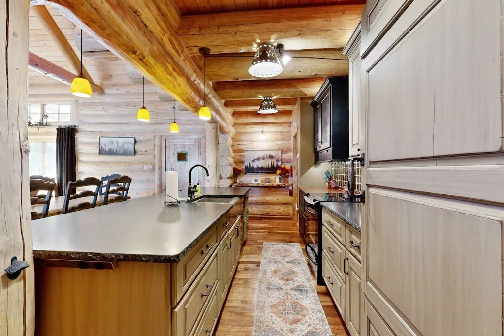 Una cocina rústica con una larga encimera central, muebles de madera y paredes de troncos.