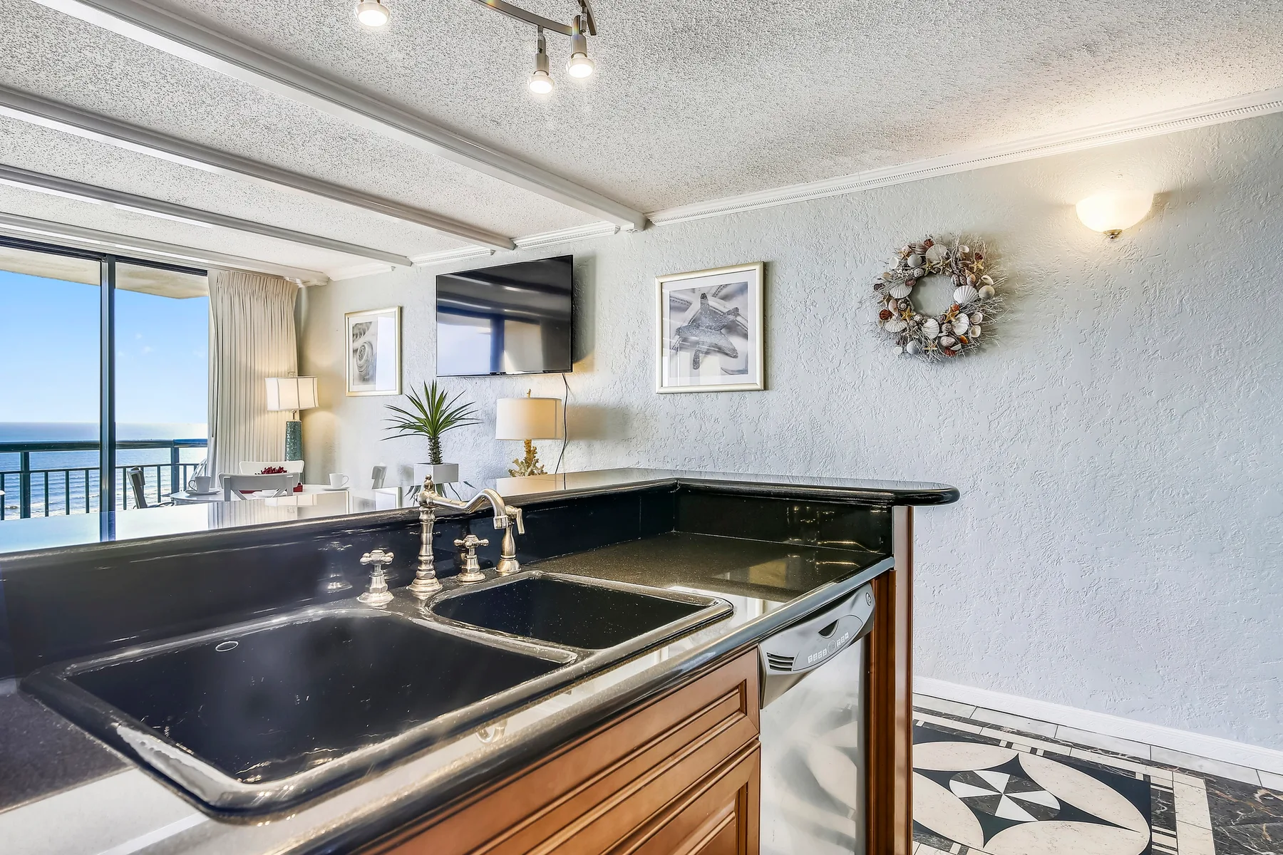 A kitchen counter with a sink overlooks a bright living area and balcony.