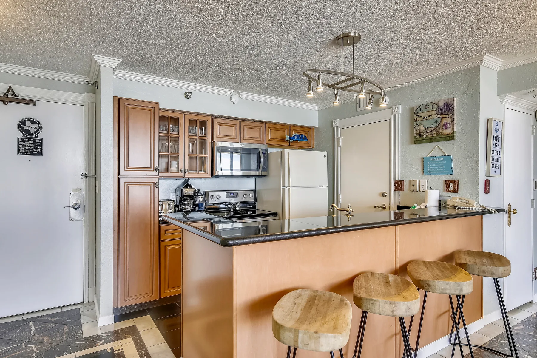 A kitchen with wood cabinetry, stainless appliances, and a breakfast bar with stools.