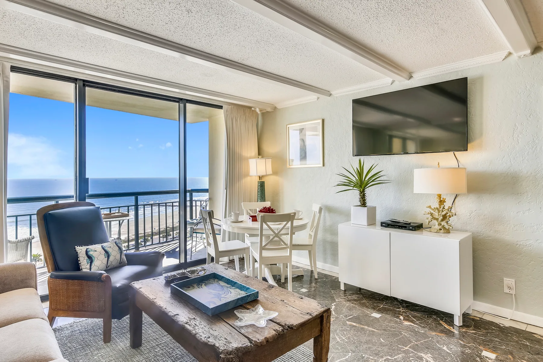 A bright living and dining area opens onto a balcony with ocean views.