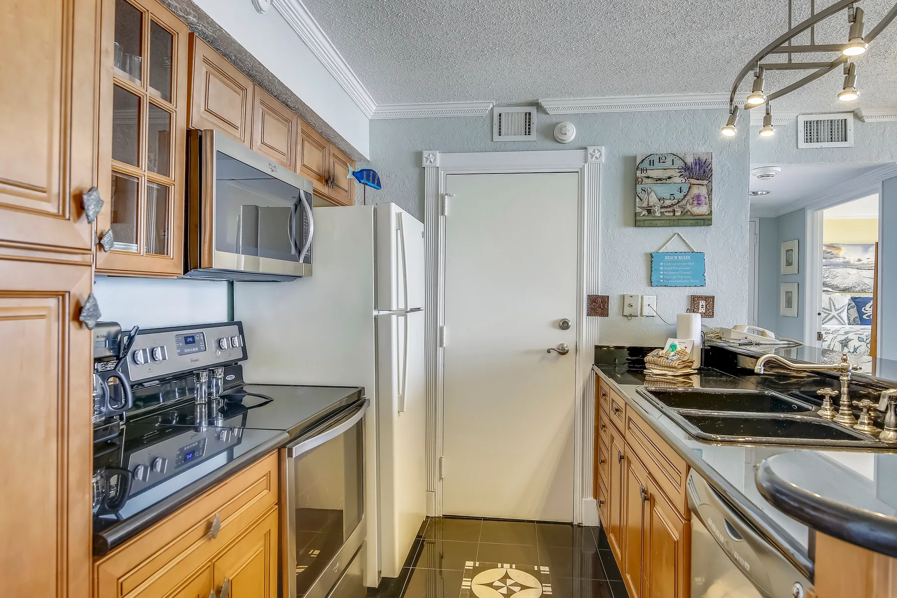 A galley kitchen with wooden cabinets, stainless steel appliances, and dark countertops.