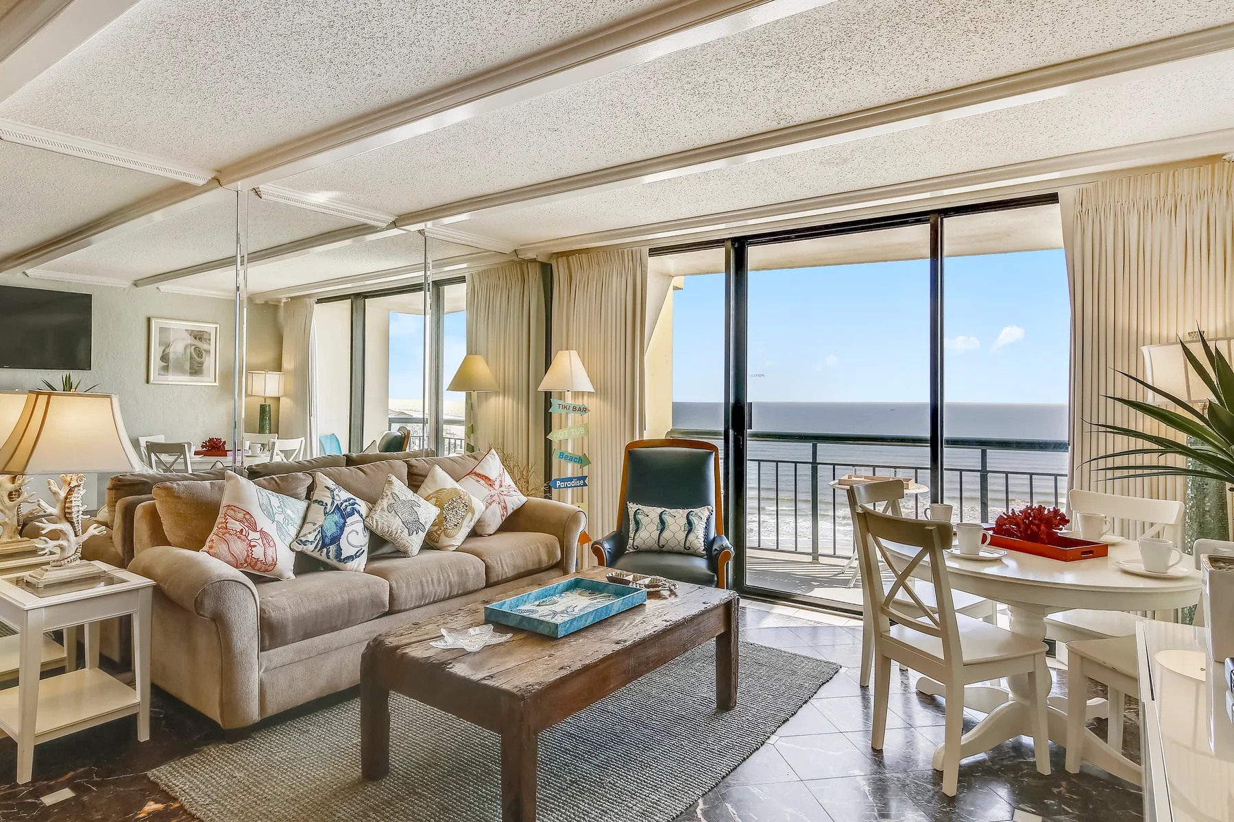 A living and dining area opens onto a balcony with a view of the ocean.