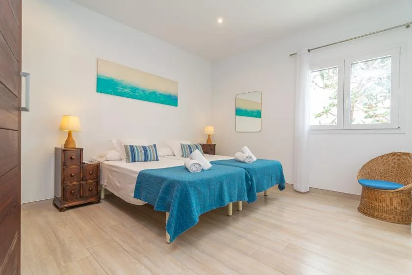 Un dormitorio luminoso con dos camas vestidas de azul y una ventana.