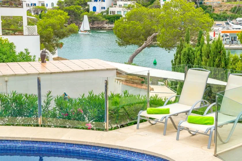 A poolside terrace overlooks a green waterfront with boats and buildings.