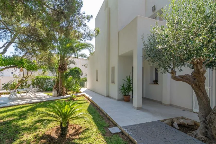 Un edificio blanco moderno da a un jardín con árboles y un camino pavimentado.
