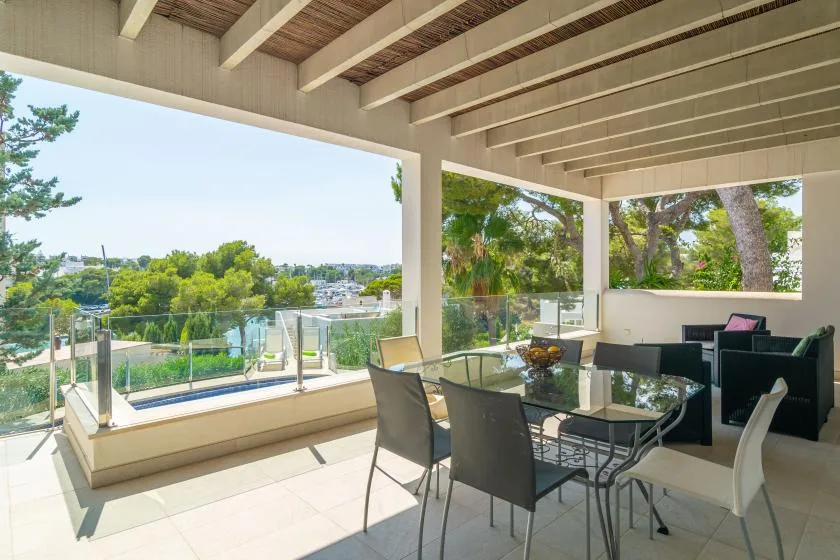 Un comedor exterior cubierto ofrece vistas a la vegetación y una piscina.