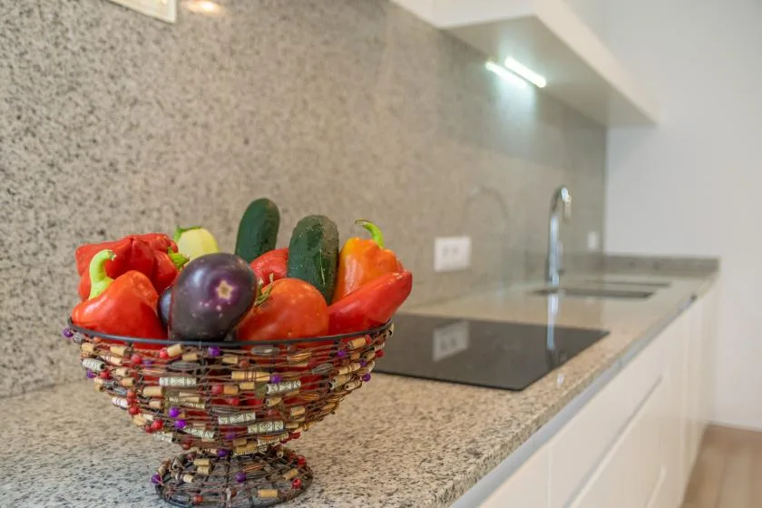 Una encimera de cocina tiene una cesta de verduras coloridas junto a una placa de cocción.