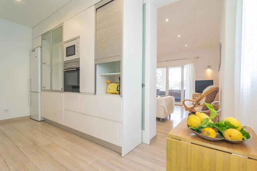 Una cocina luminosa se abre a una sala de estar, con un frutero sobre la encimera.