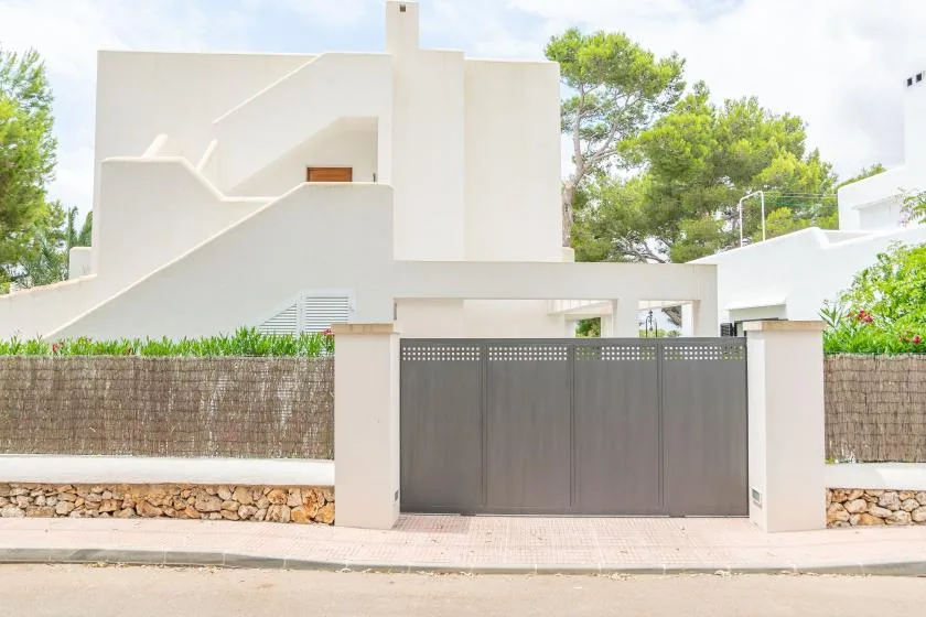 Un edificio blanco moderno se alza detrás de una alta puerta de entrada gris.
