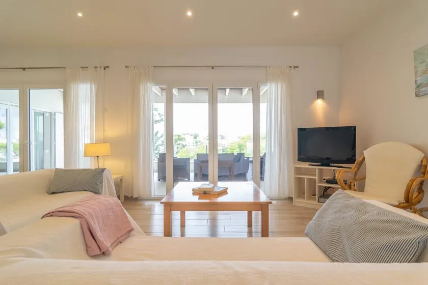 Una luminosa sala de estar con asientos, un televisor y puertas de vidrio que dan a un patio.