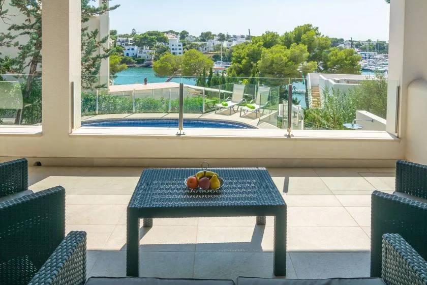 Una zona de estar en el patio da a una piscina, vegetación y casas junto al agua.