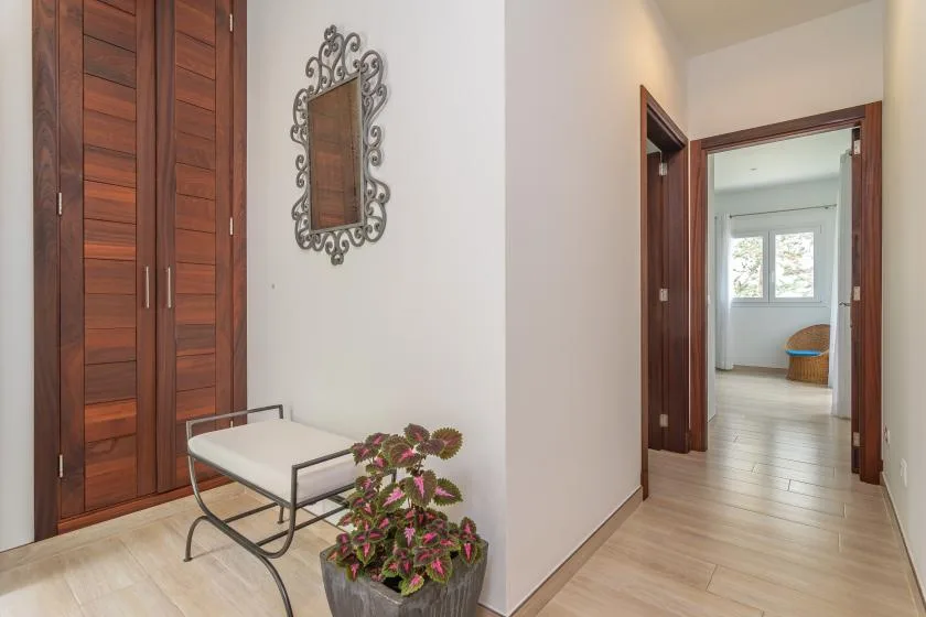 Un pasillo luminoso con puertas de madera, un asiento pequeño y flores en maceta.
