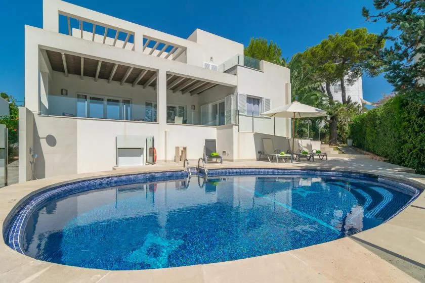 Una casa blanca moderna da a una piscina curva y una zona de estar exterior.