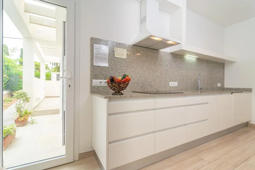 Una cocina moderna y luminosa con gabinetes blancos, salpicadero de piedra y una puerta que da a un patio.