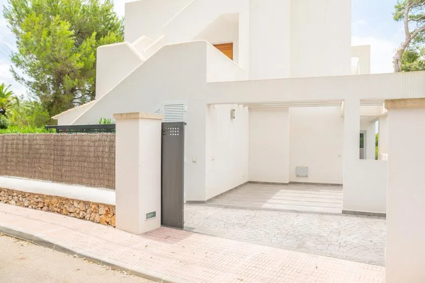 La entrada de un edificio blanco da a un acceso pavimentado junto a un muro bajo.