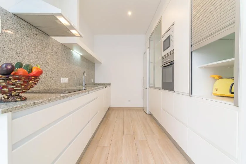 Una cocina estrecha y luminosa con gabinetes blancos y una encimera.