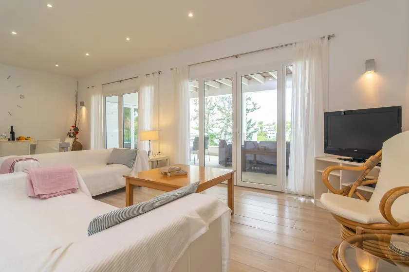 Un dormitorio luminoso con camas blancas, un televisor y grandes puertas de cristal.