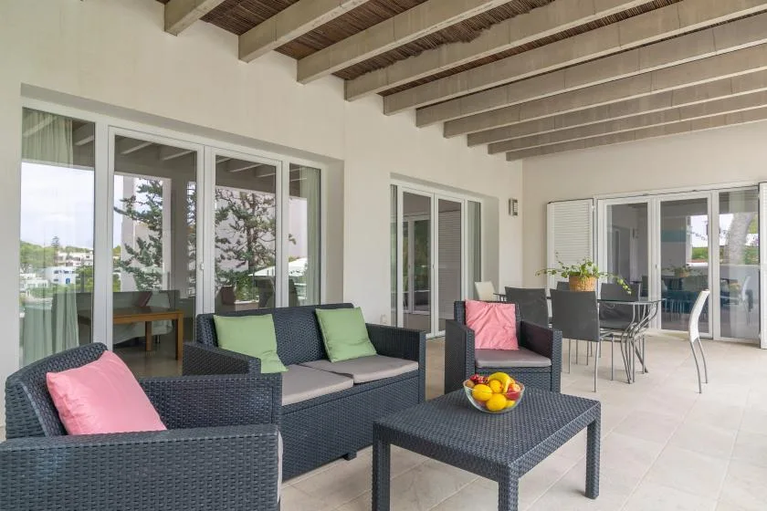Un patio cubierto con asientos de mimbre oscuro y puertas de vidrio que dan al interior.