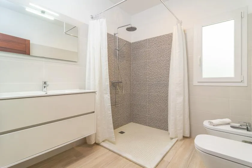 Un baño luminoso con ducha y un mueble de lavabo blanco.
