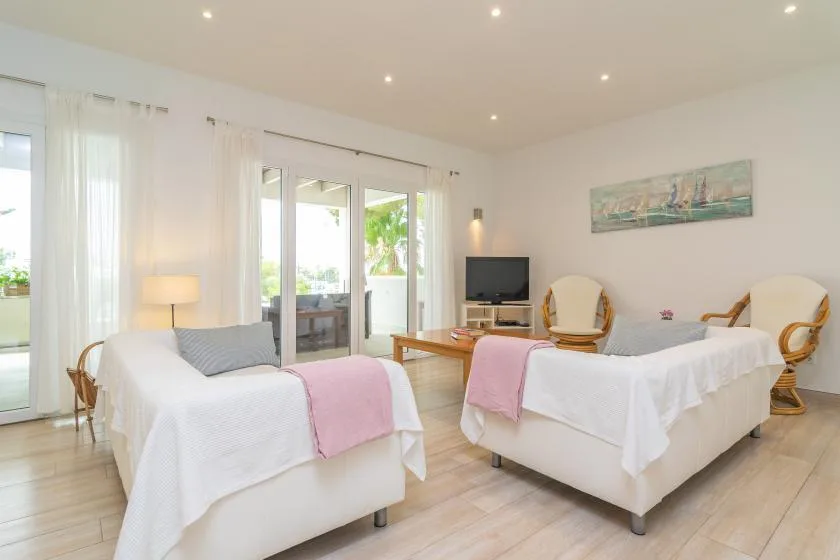 Un dormitorio luminoso con dos camas, asientos y grandes puertas de vidrio que dan a un patio.