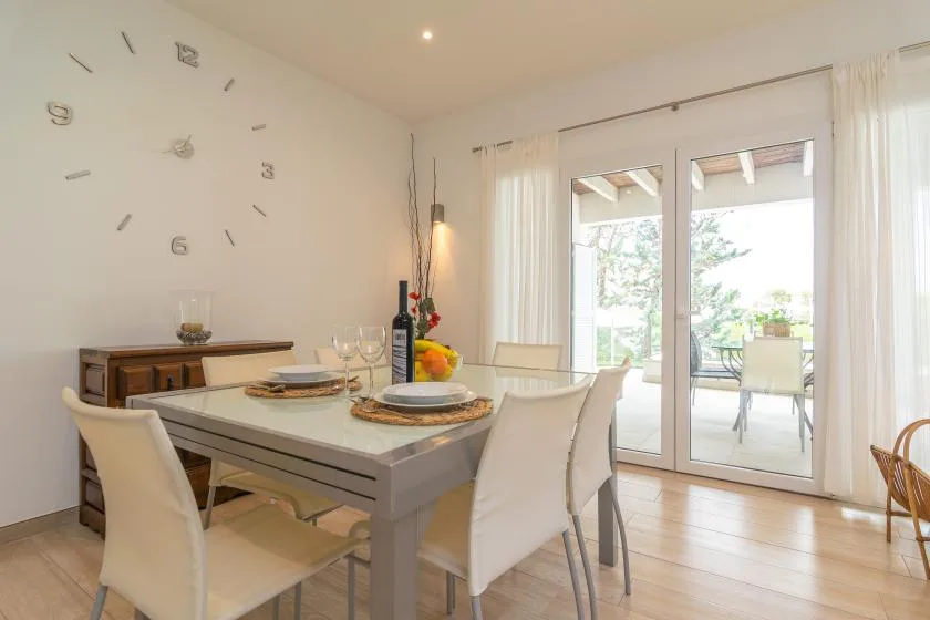 Un comedor luminoso tiene una mesa puesta junto a puertas de cristal que dan a un patio.