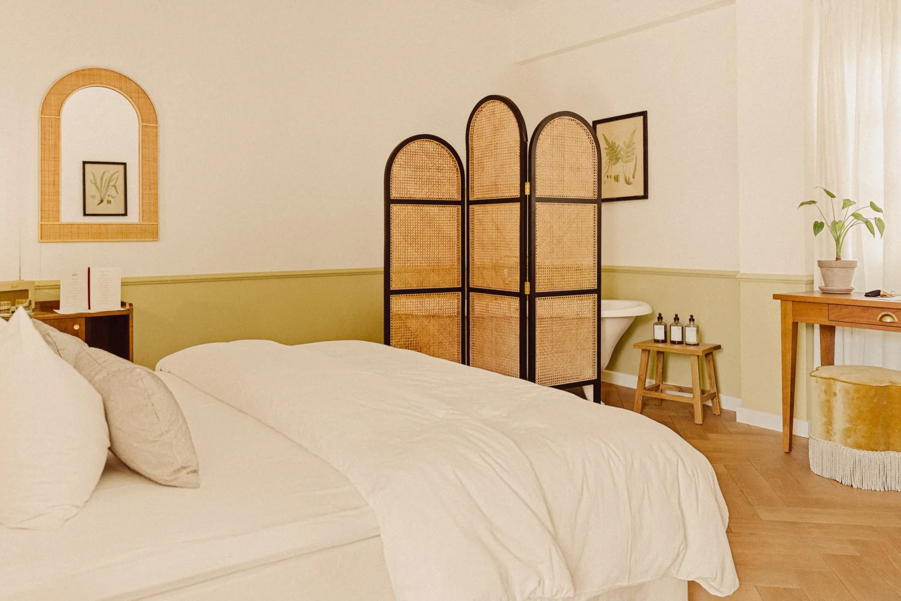 Dormitorio con una cama grande, un separador de ambientes tejido, un escritorio y obras de arte de temática botánica.