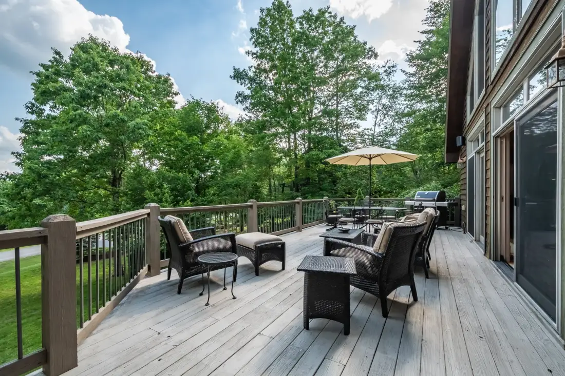 A wooden deck with outdoor seating and an umbrella overlooks leafy trees.