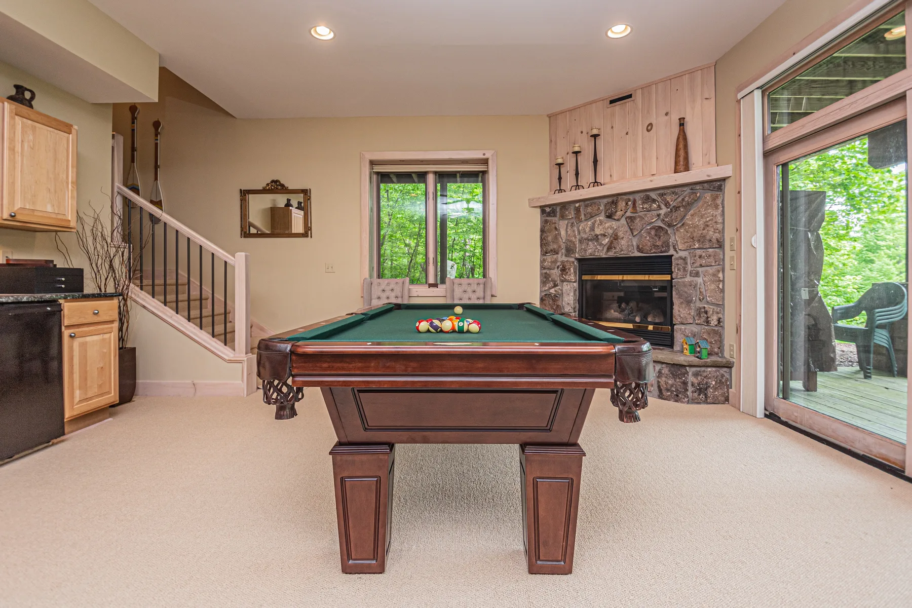 A billiards table sits in a carpeted room beside a stone fireplace.